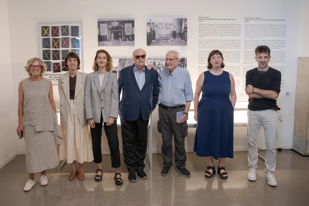Siete personas posan de pie en la sala de la exposición, delante del cartel de la edición de 1976, fotografías antiguas y paneles de texto