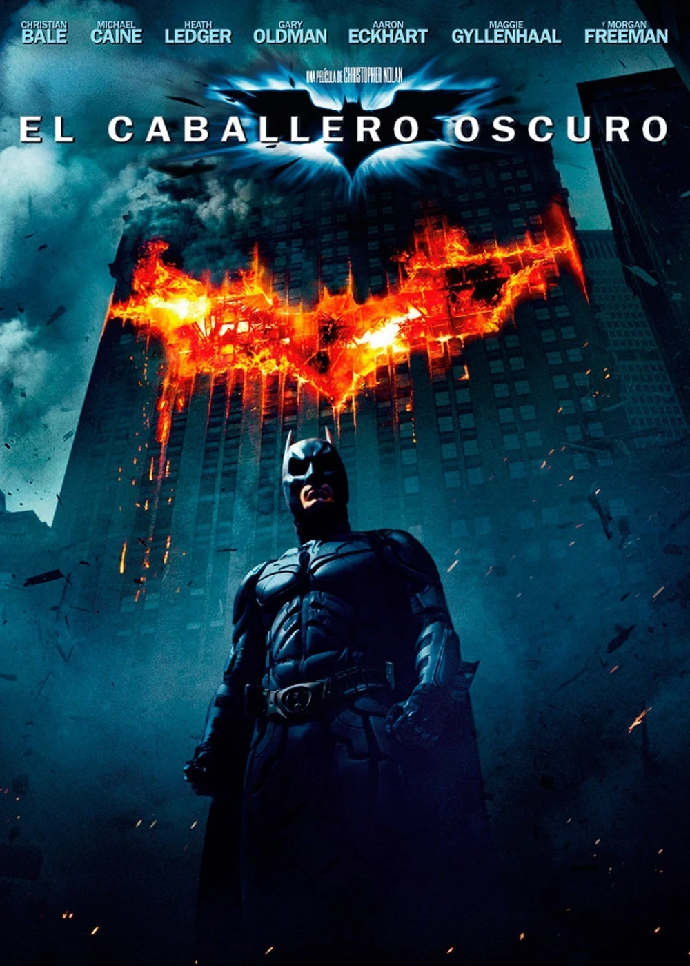 Cartel español de El caballero oscuro: Batman, de pie, ante un rascacielos en cuya fachada arde el símbolo del murciélago; arriba, el título y los nombres del reparto