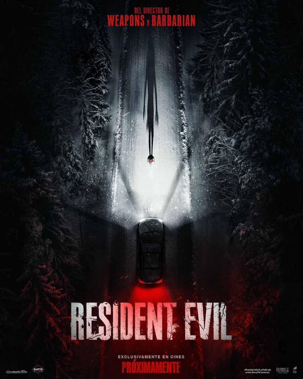 Cartel español de Resident Evil: vista cenital de un coche con los faros encendidos en una carretera nevada entre abetos; en el haz de luz, una figura solitaria proyecta una sombra larguísima