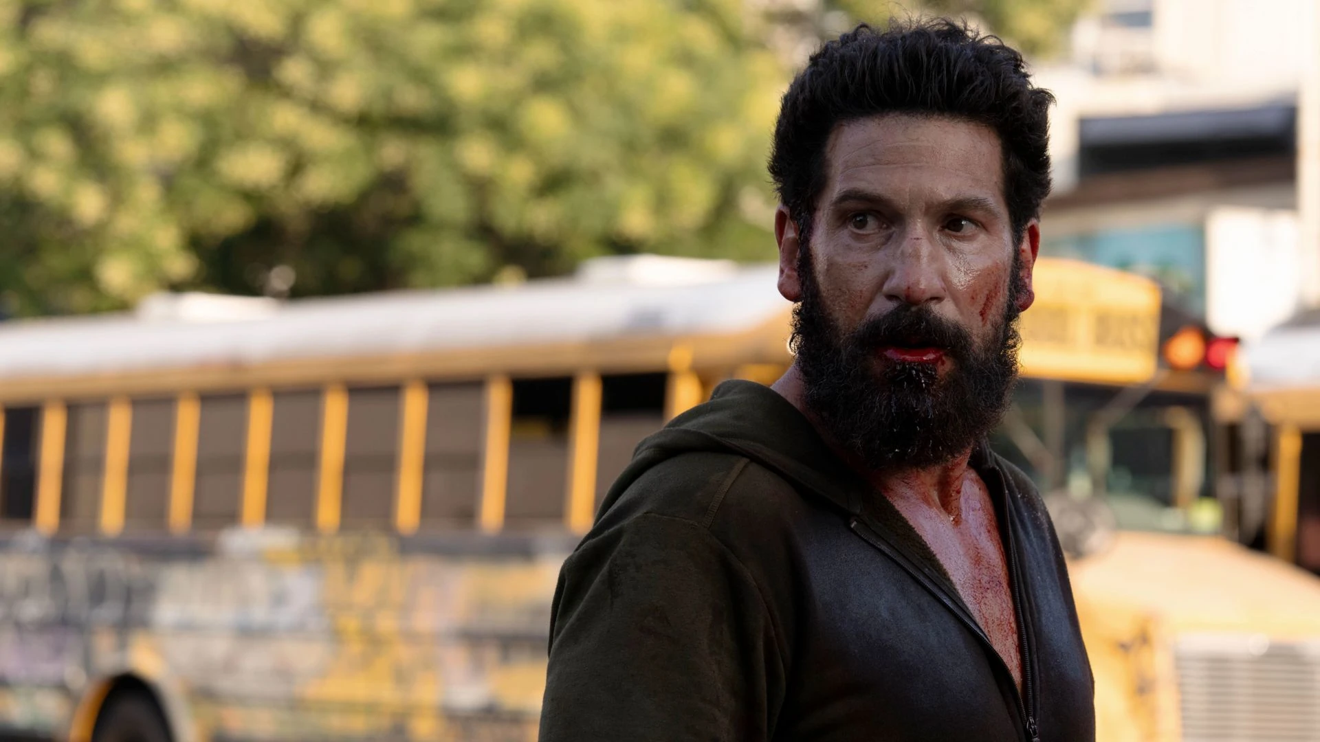 Jon Bernthal como Frank Castle, con barba y sangre en la cara, en una calle con un autobús escolar amarillo detrás