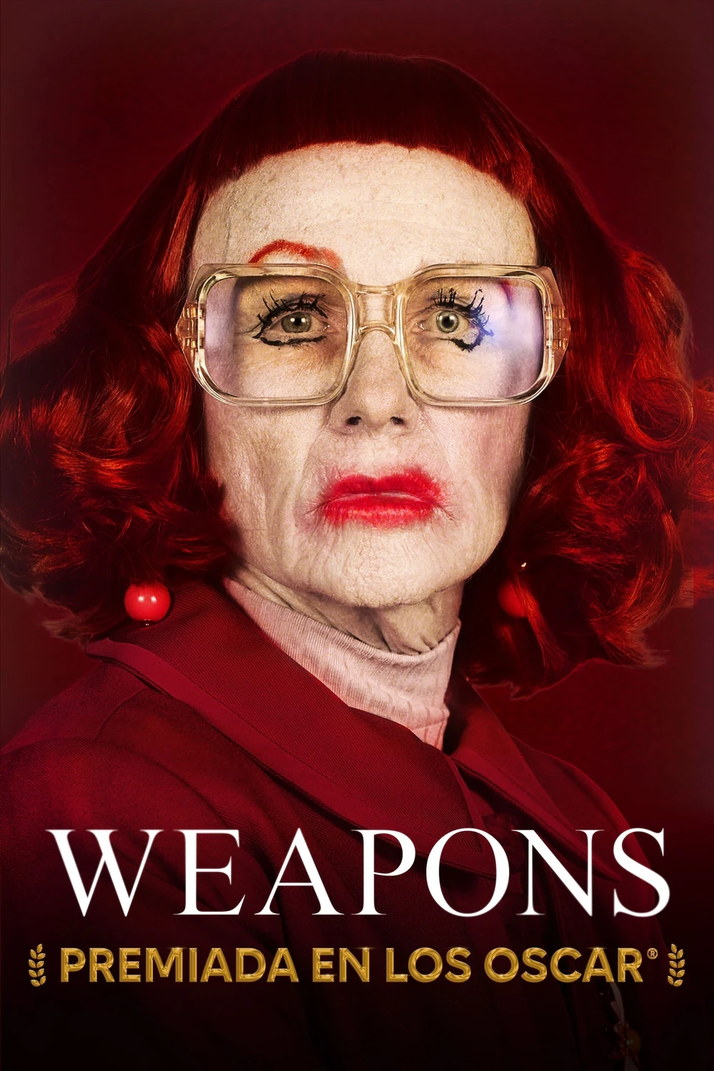 Cartel español de Weapons: primer plano de Amy Madigan con peluca pelirroja rizada, gafas grandes, labios pintados de rojo y cejas marcadas, bajo el título y la leyenda «Premiada en los Oscar»