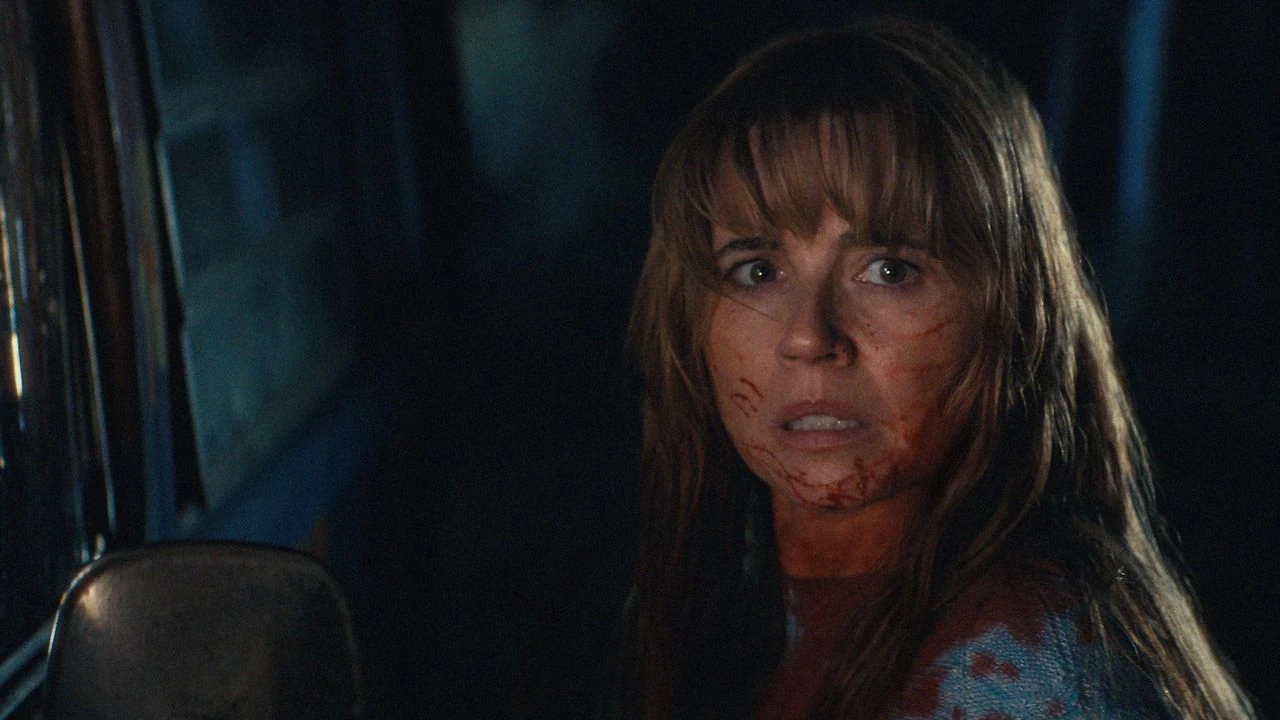 Linda Cardellini como Pamela Voorhees, de noche, con la cara manchada de sangre, mira por encima del hombro con gesto asustado