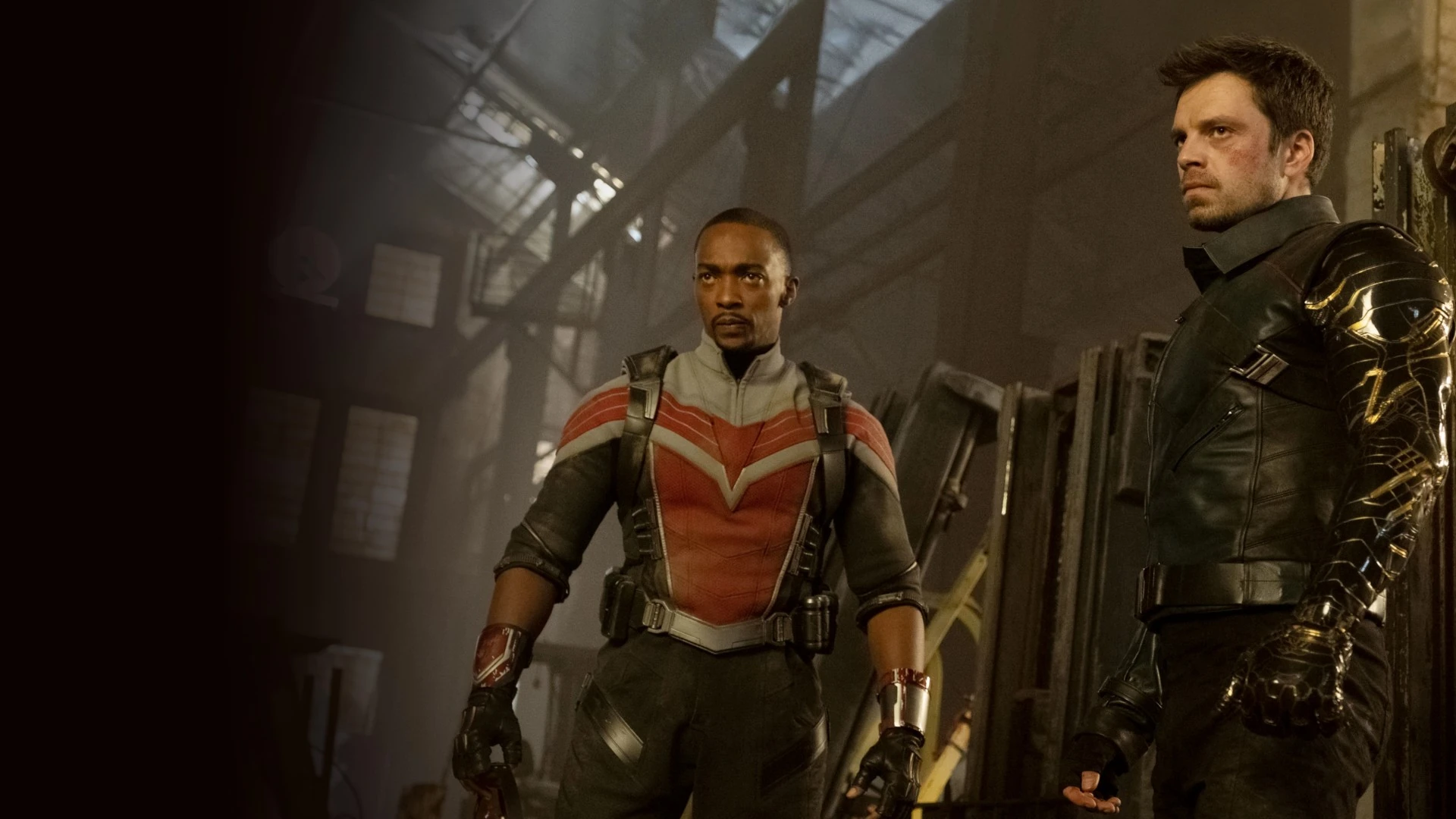 Anthony Mackie, con el traje rojo y gris de Falcon, y Sebastian Stan, con el brazo metálico del Soldado de Invierno, de pie en una nave industrial en penumbra