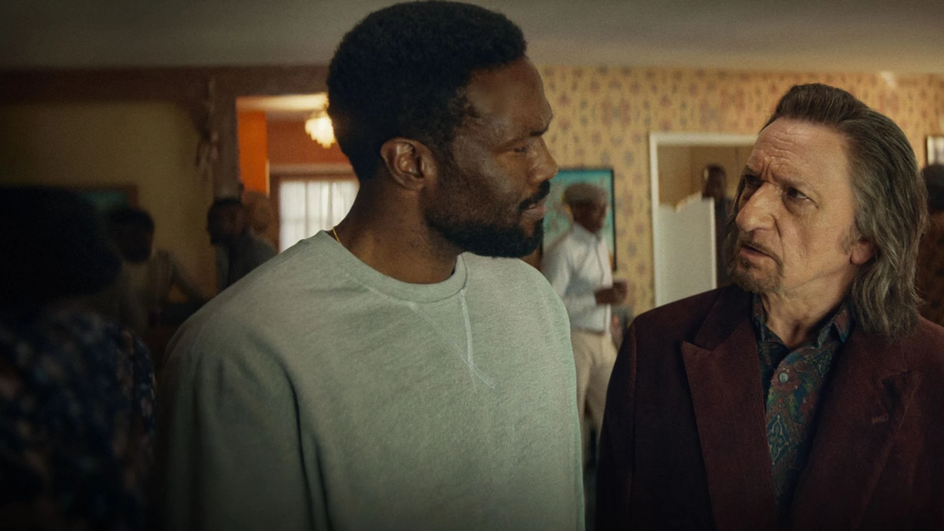 Yahya Abdul-Mateen II y Ben Kingsley, frente a frente en el salón de una casa con más gente al fondo